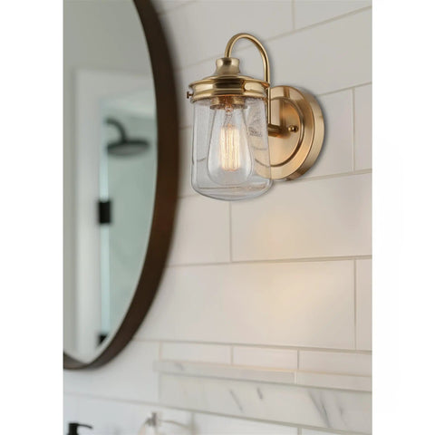Bathroom wall fixture with a brass finish and clear glass shade near mirror