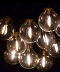 Close-up of illuminated bulbs on 25 Foot G40 Globe String Lights With 25 LED Bulbs For Indoor And Outdoor Use End To End Connectable UL Listed Candelabra E12 Sockets 12 Inch Bulb Spacing Warm White Glow For Home Decor And Commercial Events