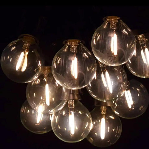 Close-up of illuminated bulbs on 25 Foot G40 Globe String Lights With 25 LED Bulbs For Indoor And Outdoor Use End To End Connectable UL Listed Candelabra E12 Sockets 12 Inch Bulb Spacing Warm White Glow For Home Decor And Commercial Events