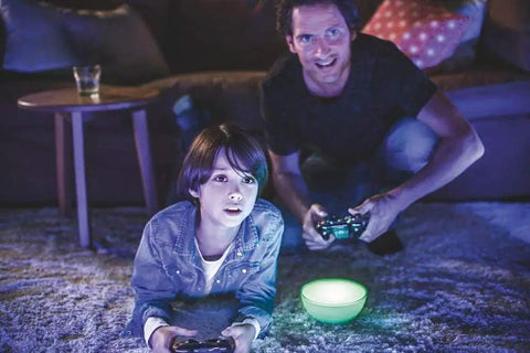 Two people gaming beside Go White And Color Portable Dimmable LED Smart Light Table Lamp That Plays Nice With Alexa HomeKit Google Assistant