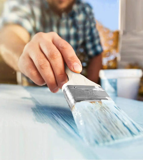 Person using Six Piece Chip Paint Brush Set With 1 Inch 2 Inch 3 Inch Natural White Bristles And Solid Wooden Ergonomic Handles for painting.