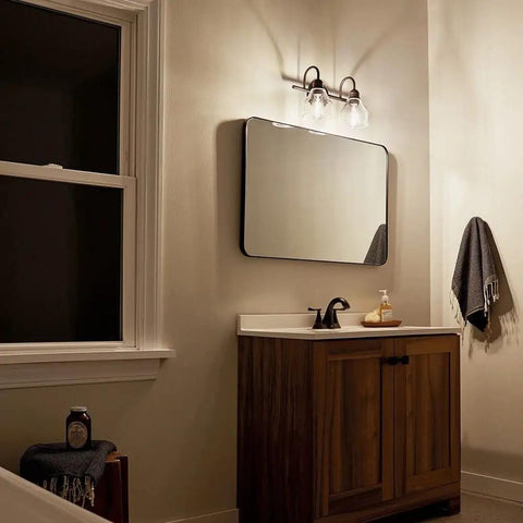 Avery 14.75 Inch Two-Light Vanity Light With Clear Seeded Glass In Olde Bronze above bathroom mirror and wooden vanity.