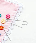 Heavy Duty Safety Pins Set By Adorainbow on pink fabric with colorful buttons, ideal for crafts and outdoor use.