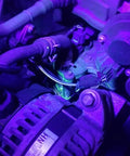 Automotive AC UV dye leak detector kit in engine bay under purple UV light