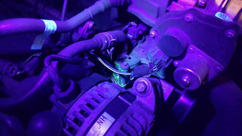 Automotive AC UV dye leak detector kit in engine bay under purple UV light