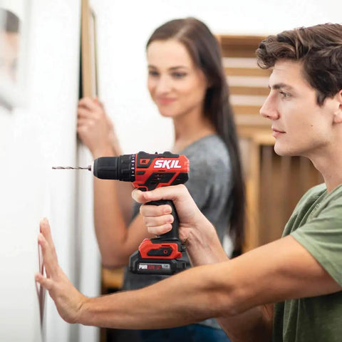 Man using Four Tool Power Pack With Brushless 12V Half Inch Drill Driver on wall, with woman assisting in background.