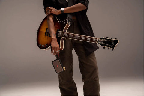 Person holding Ultra Portable 5W Smart Guitar Amp With Bluetooth Speaker Headphone Amp And Mobile App For Electric Acoustic Or Bass Guitars 33 Amps 43 Effects Custom Presets 50,000 ToneCloud Tones next to guitar.