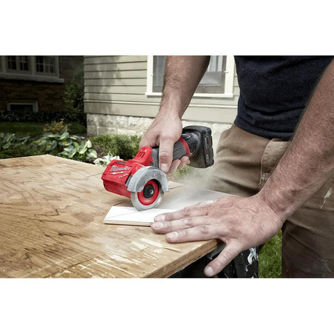 Milwaukee 12V cut-off tool, bare tool; red body with gray guard cutting a white rectangle on a wooden workbench (side view).