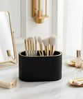 Black brush holder on marble vanity with gold accents, containing makeup brushes next to cosmetics, reflecting elegant decor.