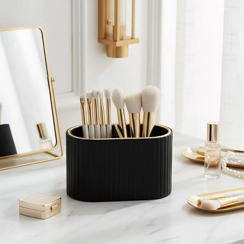 Black brush holder on marble vanity with gold accents, containing makeup brushes next to cosmetics, reflecting elegant decor.