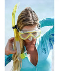 Person adjusting Vapor Semi Dry Snorkel For Snorkeling Mask And Underwater Breathing Gear With Purge Valve Easy Breathing No Fuss Comfort Optimal Clearing Lightweight Dive Snorkel For Scuba And Free Diving Black with clear snorkel mask, wearing turquoise swim gear on a beach