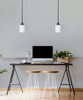 Modern workspace with two pendant lights over desk, plants, and stools, showcasing sleek interior design.