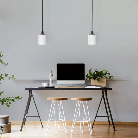 Modern workspace with two pendant lights over desk, plants, and stools, showcasing sleek interior design.