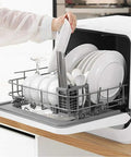 Compact Countertop Dishwasher With Six Place Settings And Five Wash Cycles Makes Kitchen Cleanups A Total Breeze For Small Apartments And Busy Homes, holding plates and utensils.