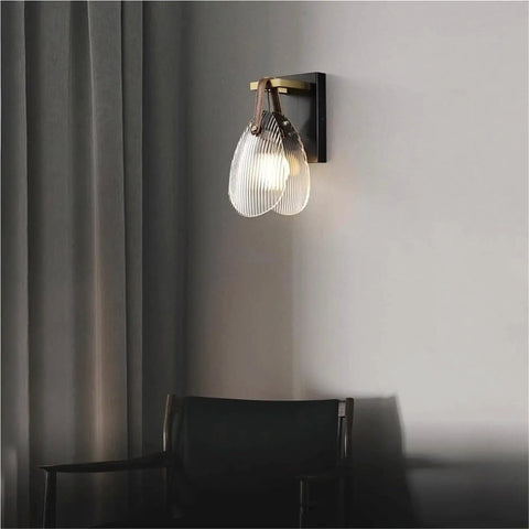Fluted Glass Wall Sconce Ribbed Shade Leather Strap Brass Finish Metal Light 10 Inch Height mounted on wall beside chair.