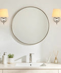 1-Light Brushed Nickel Vanity Light with Beige Fabric, Modern Wall Sconce beside a round mirror and vanity sink.