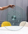 Top Shelf Thick Tempered Glass Lazy Susan Rotating Serving Tray Easy Peasy Clean Spinner held above a dining table.