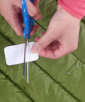 Person cutting fabric patch from Tenacious Tape Mini Patches With Peel And Stick Adhesive For Holes And Tears In Winter Gear