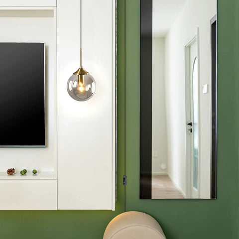 Mid Century Modern Brushed Gold Pendant Light With Plug In Cord, Smoke Gray Glass Globe hanging in living room next to mirror.