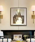 Two Pack Brushed Brass Wall Sconces With Fabric Shade in living room setting, wall mounted beside artwork, gold finish.