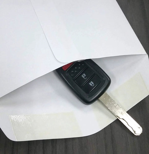 Front view of white 6x9 in key drop envelope with gummed seal and car key for scale