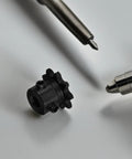 9 Tooth Single Strand Roller Sprocket Made Of Tough Carbon Steel For Smoother Power Transmission Plus Noise Reduction In Humid Or Dusty Shop Floors And Jobsites on gray surface with pen nearby.