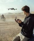 Person controlling Mavic 3 Cine Premium Drone Kit With Hasselblad 4/3 CMOS Camera in desert near motorcyclist
