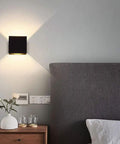 Bedroom setting with Dimmable 10W LED Indoor Wall Sconce in Black Finish, modern square design, casting up and down warm white light.