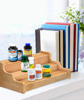 Expandable 3 Tier Bamboo Spice Rack And Kitchen Cabinet Organizer fits standard jars horizontally displaying vitamins and books.