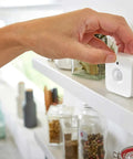 Person installing Indoor Smart Motion Sensor 2 Pack With Daylight Sensing on shelf, compact white sensor in hand.