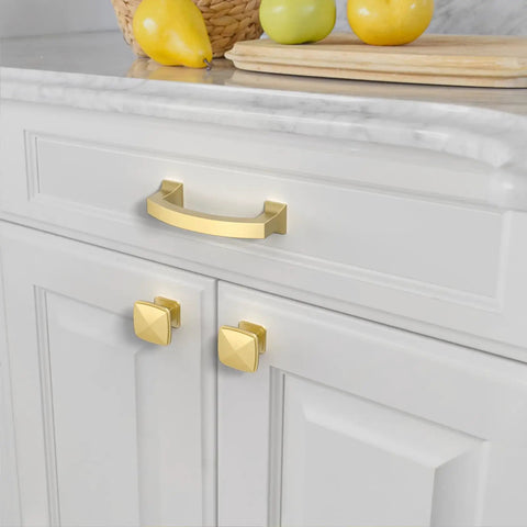 Gold cabinet handles on a white kitchen cabinet next to fruit on counter