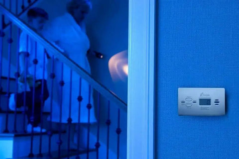 Carbon Monoxide Detector With Ten Year Battery Digital Display Three LEDs Replacement Indicator Peak Level Memory Two Pack For Easy Home Safety No Wiring Needed And It Alerts On Power Outage With An 85 Decibel Alarm mounted on wall near stairs.