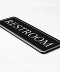 Premium Restroom Sign 9x3 Acrylic With Double Sided 3M Tape HD UV Print Bright Black Background Easy To Find No Fuss Restroom Recognition In Hotels Cafes And Offices, angled view.