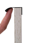 Close-up of black aluminum edge pull handle with concealed tab, part of 10 Pack Black Aluminum Edge Pull Handles Hidden Concealed Tab Pulls For Doors Drawers Cabinets Wardrobes Sleek 80mm And 3.2 Inch Finger Pulls Durable Modern Hardware For Home, being held by finger on wood surface.