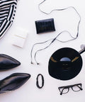 Flat lay of fashion items including striped dress, black shoes, glasses, vinyl record, and accessories on a white background.
