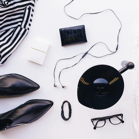 Flat lay of fashion items including striped dress, black shoes, glasses, vinyl record, and accessories on a white background.