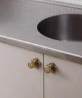 Top Shelf Antique Brass Cabinet Knobs With Quatrefoil Backplate on white cabinet under stainless sink.