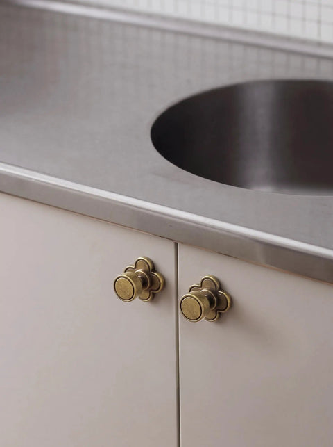 Top Shelf Antique Brass Cabinet Knobs With Quatrefoil Backplate on white cabinet under stainless sink.