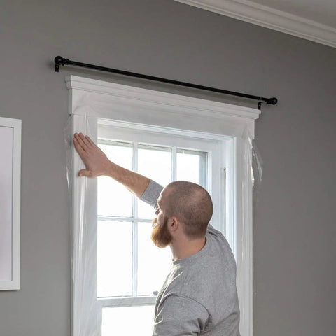 Person applying Indoor Three Window Shrink Film Insulator Kit With Crystal Clear Film 62 By 126 Inches Includes 54 Feet Double Sided Tape Stops Drafts And Saves Big On Energy Bills Easy Home Weatherproofing For Maximum Comfort to window frame.