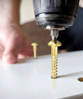 Brass Round Head Wood Screws M3 X 25mm Slotted Self-Tapping being installed into wood with a drill, close-up view.