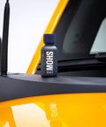 GYEON MOHS ceramic coating bottle with blue cap on car dashboard beside a yellow exterior panel