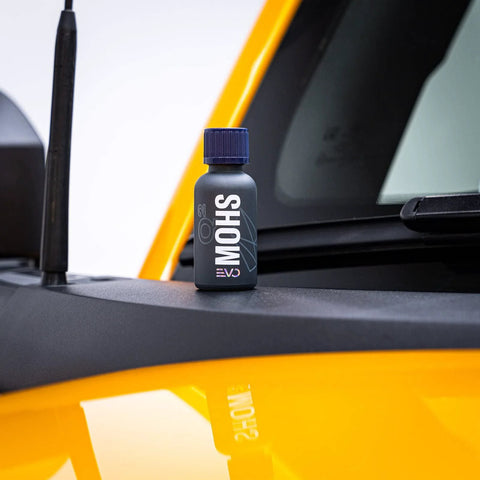 GYEON MOHS ceramic coating bottle with blue cap on car dashboard beside a yellow exterior panel
