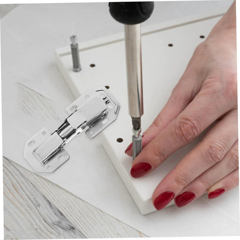 Two silver hydraulic cabinet hinges being installed on a white kitchen cabinet panel; screwdriver in use.