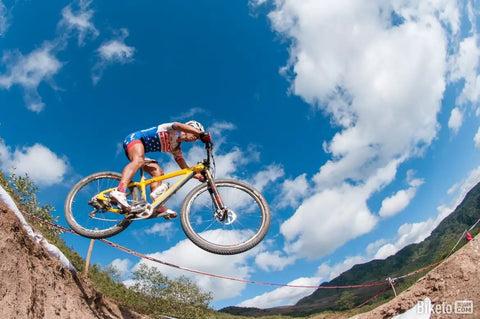 Mountain biker mid-air during a race on a trail under blue sky