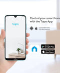 Hand holding a smartphone displaying Tapo app interface for smart home control, with app store logos for iOS and Android.