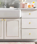 Kick The Look Upgrade With Solid Round Cabinet Knobs And Smooth Drawer Pulls In Dope Brushed Gold Finish on a white bathroom vanity.