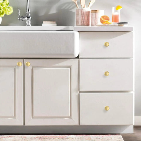 Kick The Look Upgrade With Solid Round Cabinet Knobs And Smooth Drawer Pulls In Dope Brushed Gold Finish on a white bathroom vanity.