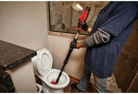 User operating Badass 12V M12 Ready Drain Snake And Toilet Auger Combo Kit on a toilet for effective clog removal.