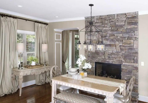 Dining room with stone wall, white table, and modern ceiling light fixture for entertaining, featuring Topsail three light inverted pendant.