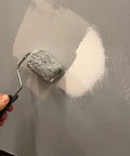 Hand using a paint roller on a patched wall after using the Drywall Repair Kit With Tapered Hole Saw And Two Plugs For Clean Flat Patches.